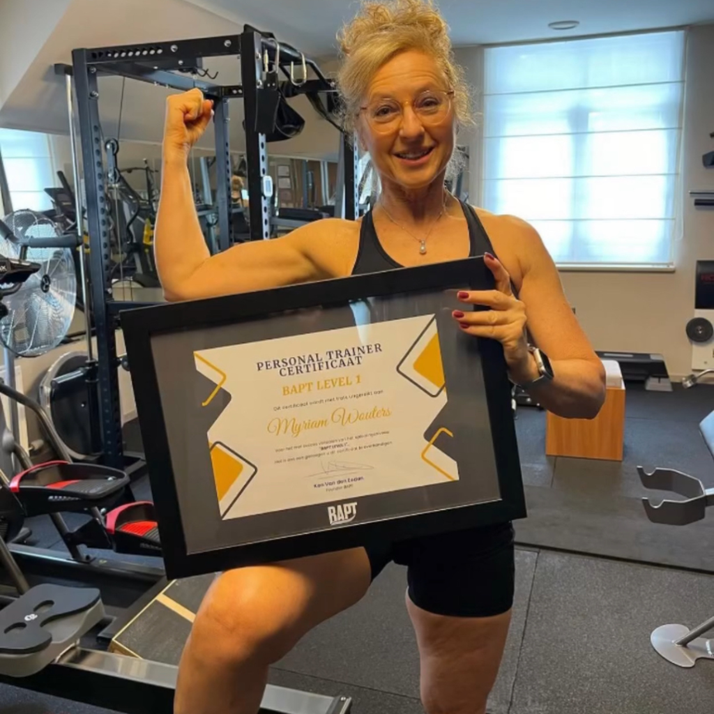 Vrouw in een sportschool houdt een ingelijst personal trainer-certificaat vast en spant haar arm