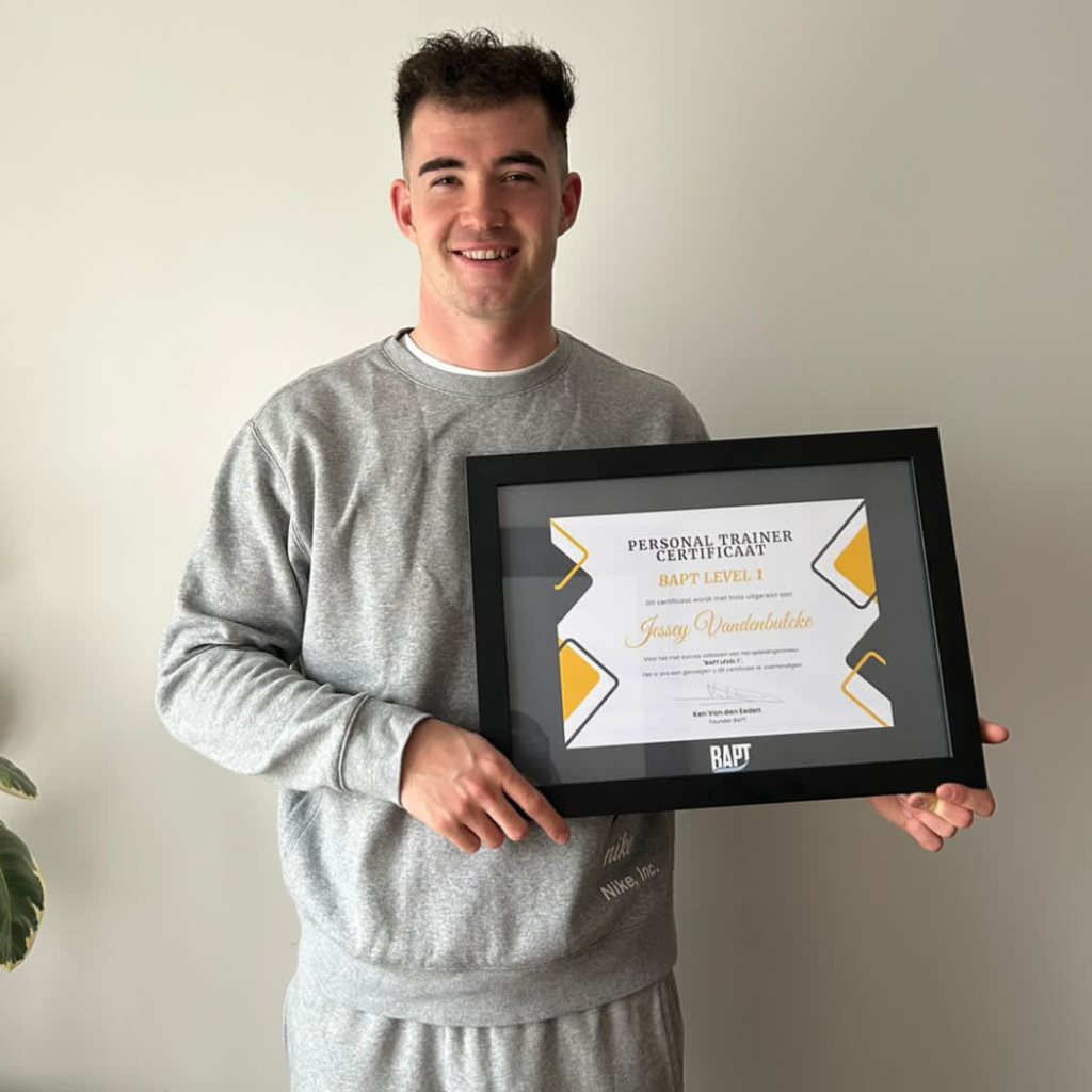 Jonge man houdt een ingelijst personal trainer-certificaat vast en glimlacht